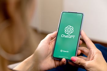 A woman holding a cell phone and the screen shows ChatGPT